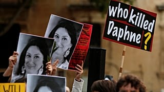People hold up photos of assassinated anti-corruption journalist Daphne Car