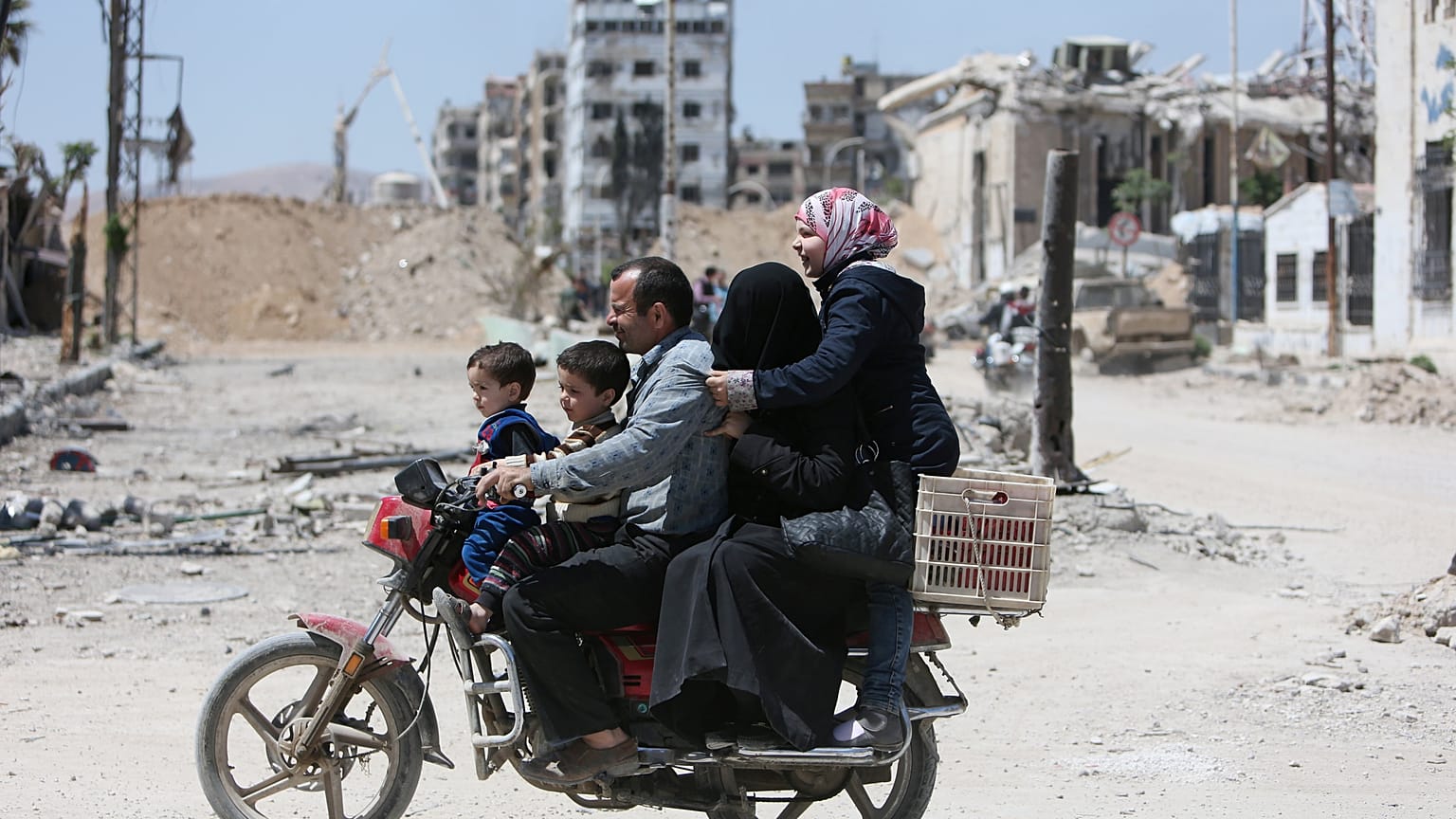 A Syrian family rides along a damaged street in Douma, Damascus.