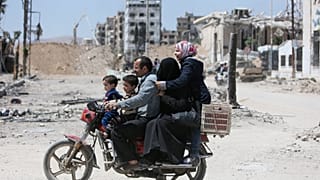 A Syrian family rides along a damaged street in Douma, Damascus.