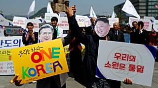 People hold hands as they wear masks of South Korea's President Moon Jae-in
