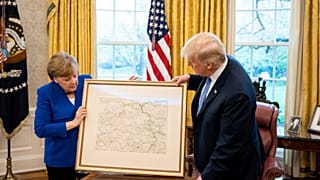Merkel übergibt Trump eine Landkarte von Rheinland-Pfalz.