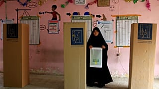 Eine Frau mit Stimmzettel neben den Wahlkabinen im Irak