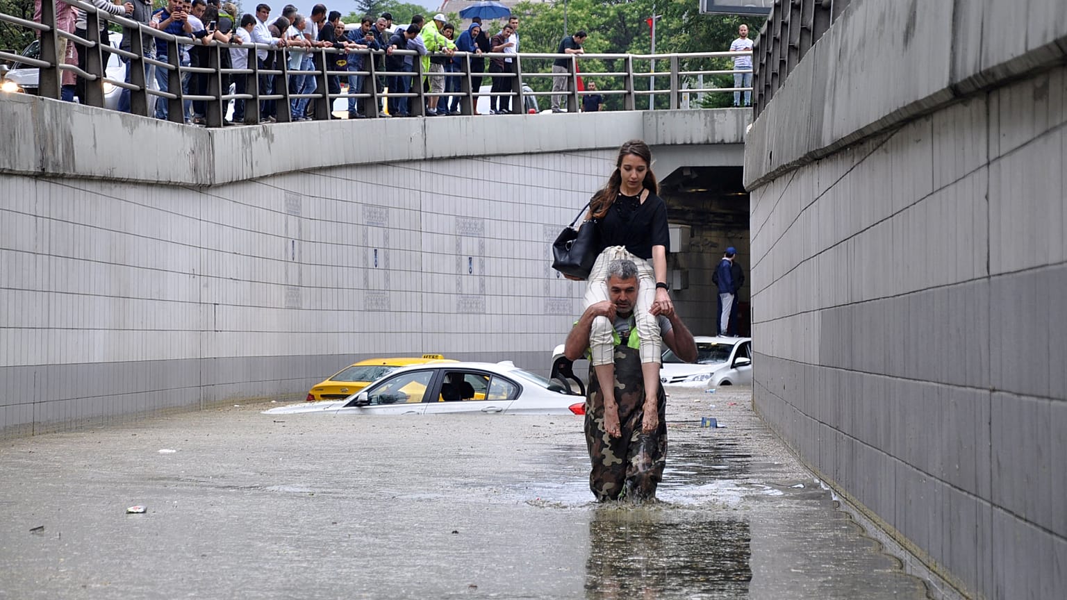 Man carries a woman on his shoulders at a flooded street