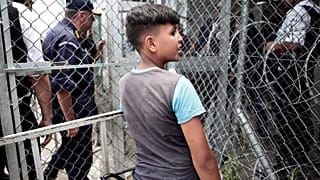 A migrant boy stands next to a fence at the Moria refugee camp on Lesbos.