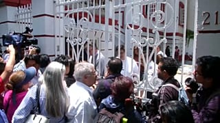 Mexikaner warten an weißem Gittertor auf Einlass