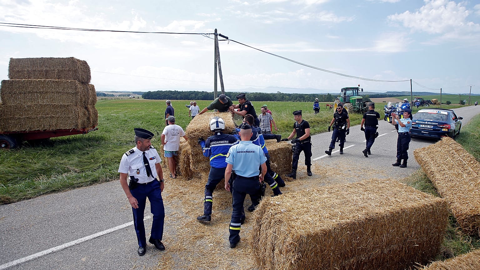 Police clear bales of straw from the path of the Tour de France