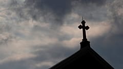 Kreuz auf Kirchendach vor dunklen Wolken