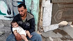فلسطيني يحمل طفلا داخل مخيم للاجئين في غزة يوم السبت.