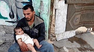 فلسطيني يحمل طفلا داخل مخيم للاجئين في غزة يوم السبت.