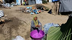 A migrant empties water into a bucket at a makeshift camp in Greece