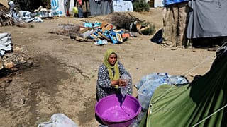 A migrant empties water into a bucket at a makeshift camp in Greece