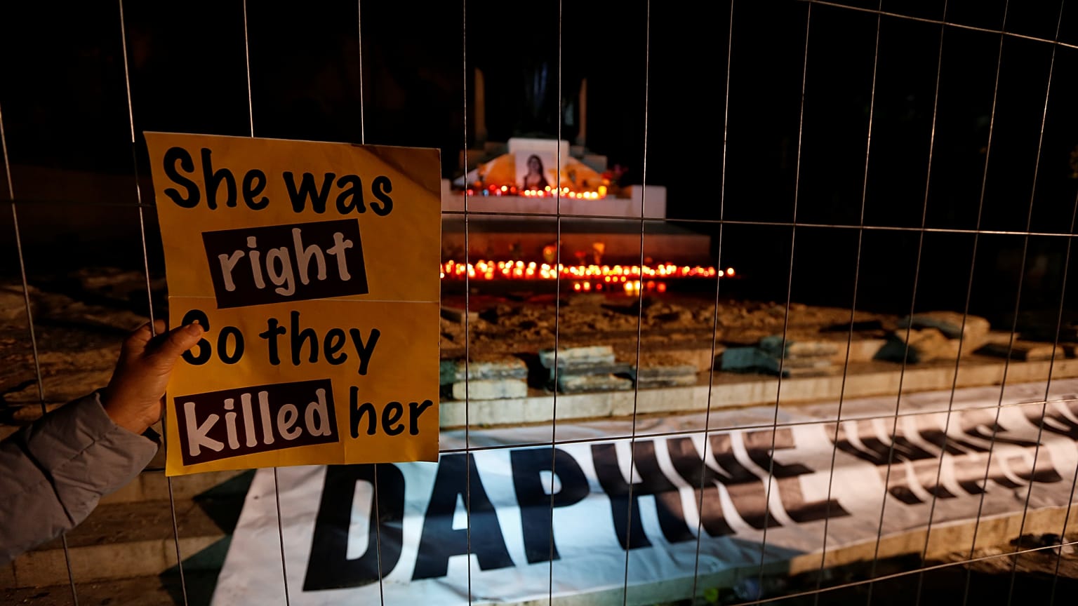 Plakat "She was right, so they killed her" vor Kerzen
