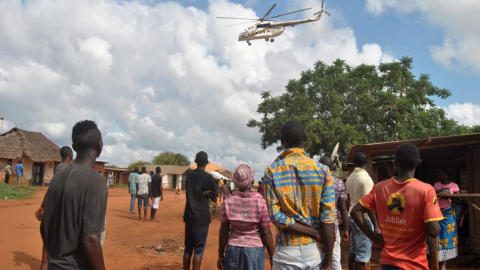 Residents look at a police helicopter patrolling the area