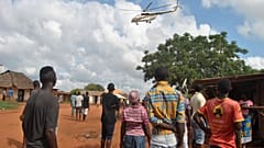 Residents look at a police helicopter patrolling the area