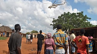 Residents look at a police helicopter patrolling the area