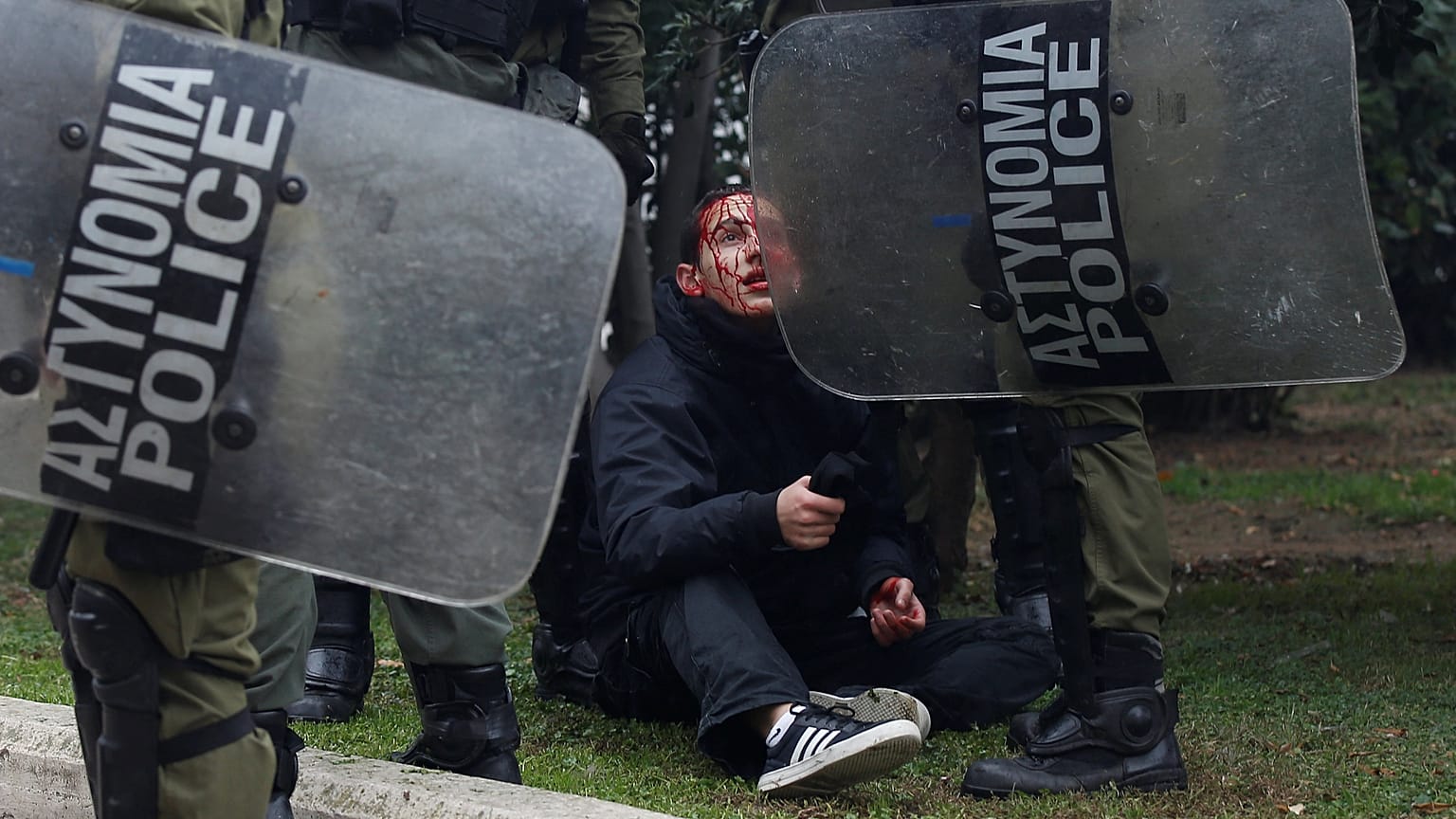 Ein verletzter Demonstrant wird von griechischen Polizisten festgehalten.