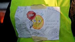 A protester wears a yellow vest bearing the slogan "don't give up."