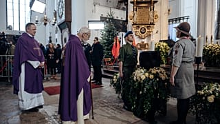 Scouts and clergy members stand near the remains of the city's mayor 