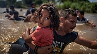 Ein Migrant aus Honduras hilft einem Kind über einen Fluss.