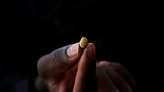 Eine Hand hält ein kleines Goldkorn zwischen den Fingern