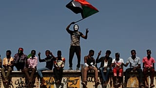 متظاهر سوداني يرتدي قناعا ويلوح بالعلم الوطني