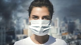 Air pollution in the city. Woman wearing face mask for protection.