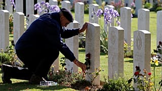 A man places a flower on a tomb at Commonwealth War Cemetery in Bayeux