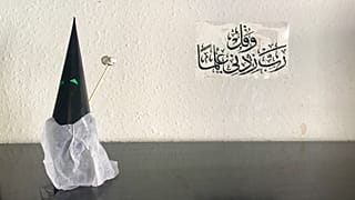 Capirote de Semana Santa hecho con papel.Al fondo, una inscripción coránica