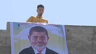 شاب يقوم بتعليق صورة كبيرة لرئيس مصر السابق محمد مرسي على حافة بناء في رفح بقطاع غزة