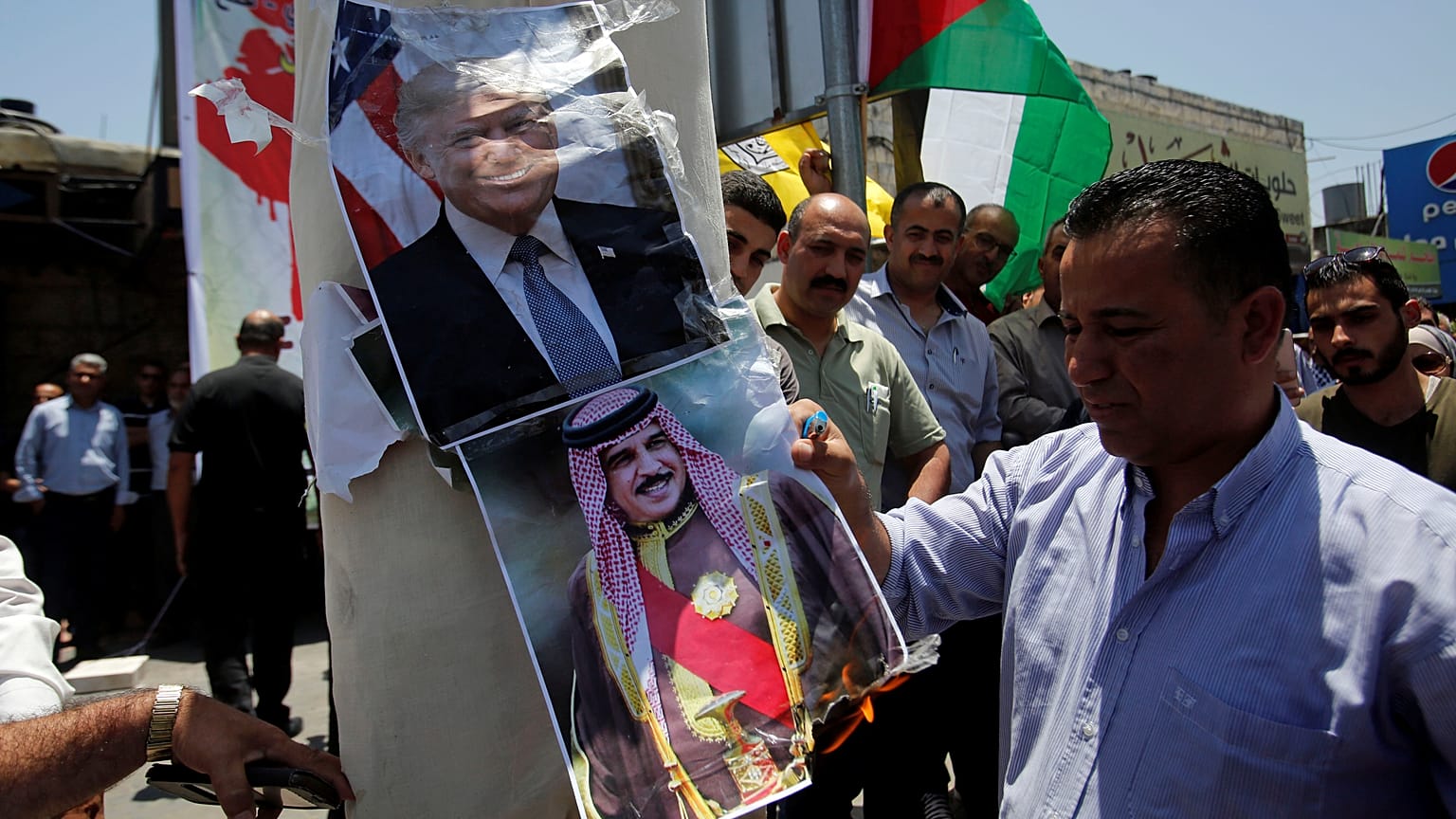 A Palestinian demonstrator burns posters depicting Bahrain's King Hamad bin Isa Al Khalifa and U.S. President Donald Trump during a protest against the Bahrain conference