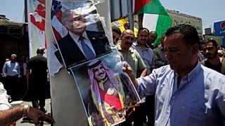A Palestinian demonstrator burns posters depicting Bahrain's King Hamad bin Isa Al Khalifa and U.S. President Donald Trump during a protest against the Bahrain conference