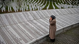 Una mujer reza cerca de la placa conmemorativa con nombres de fallecidos en la masacre de Srebrenica, antes de ver el juicio en el tribunal de La Haya, en Potocari.