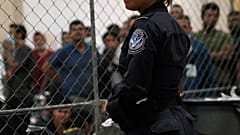 Single men wait behind caged wire at a detention facility in Texas on Friday