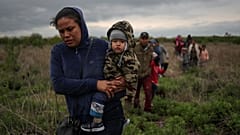 Ana María, de El Salvador, lleva en brazos a su hijo de un año, Mateo, mientras caminan por un campo con otros inmigrantes centroamericanos que buscan asilo.