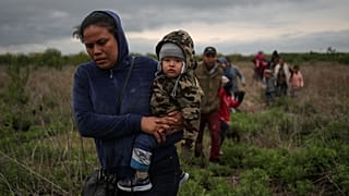 Ana María, de El Salvador, lleva en brazos a su hijo de un año, Mateo, mientras caminan por un campo con otros inmigrantes centroamericanos que buscan asilo.