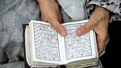 A woman prays while holding the Quran.