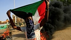 محتج ملثم يرفع علم السودان وخلفه إطارات تحترق أثناء احتجاج في العاصمة الخرطوم يوم 27 يوليو تموز 2019. تصوير: محمد نور الدين عبد الله