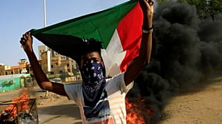 محتج ملثم يرفع علم السودان وخلفه إطارات تحترق أثناء احتجاج في العاصمة الخرطوم يوم 27 يوليو تموز 2019. تصوير: محمد نور الدين عبد الله