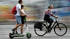 Radfahrerin überholt in Berlin zwei Verkehrsteilnehmer auf einem E-Tretroller.