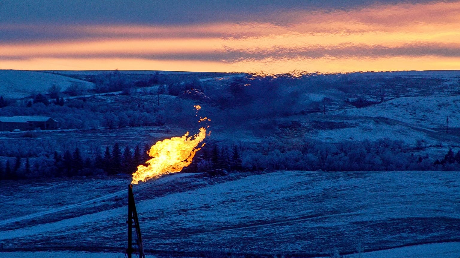 A natural gas flare on an oil well pad burns as the sun sets outside Watford City, North Dakota