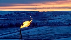 A natural gas flare on an oil well pad burns as the sun sets outside Watford City, North Dakota