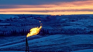 A natural gas flare on an oil well pad burns as the sun sets outside Watford City, North Dakota