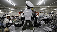 A humanoid robot works side by side with employees at a factory of Glory Ltd., a manufacturer of automatic change dispensers, in Kazo, north of Tokyo