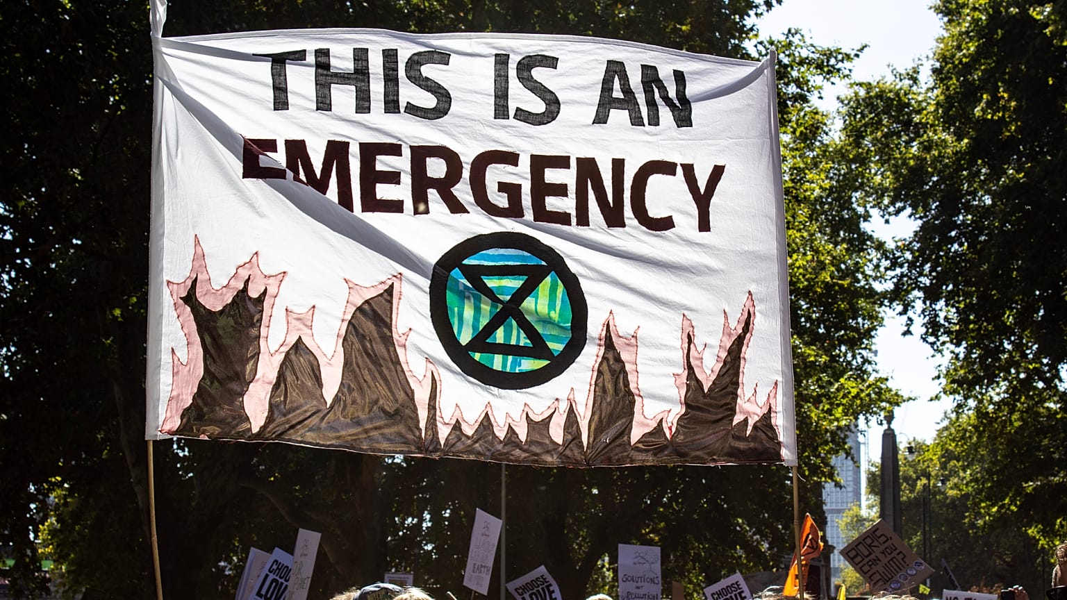 A banner declaring climate emergency alongside an Extinction Rebellion symbol is held high above the crowd
