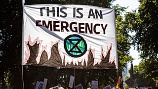 A banner declaring climate emergency alongside an Extinction Rebellion symbol is held high above the crowd