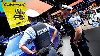 Greenpeace activist climbs on a displayed car as a sign of protest against the global warming during the visit of German Chancellor Angela Merkel to the Frankfurk Motor Show