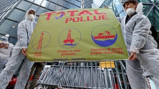 El movimiento antiglobalización Attac sostiene una pancarta frente al edificio Total mientras protestan en La Defense, cerca de París, Francia, el 12 de octubre de 2019.