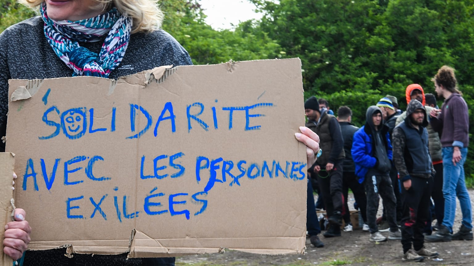 A woman holds a sign reading "Solidarity with people in exile" as she takes part in a solidarity march in support of migrants, in Calais, northern France on May 8, 2019.