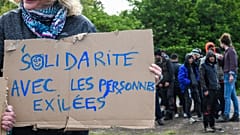 A woman holds a sign reading "Solidarity with people in exile" as she takes part in a solidarity march in support of migrants, in Calais, northern France on May 8, 2019.