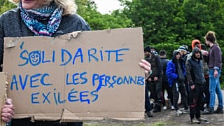 A woman holds a sign reading "Solidarity with people in exile" as she takes part in a solidarity march in support of migrants, in Calais, northern France on May 8, 2019.